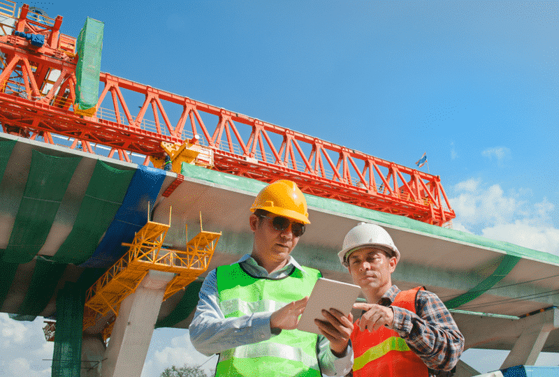 Bridge construction workers outside reading a tablet in the sunlight